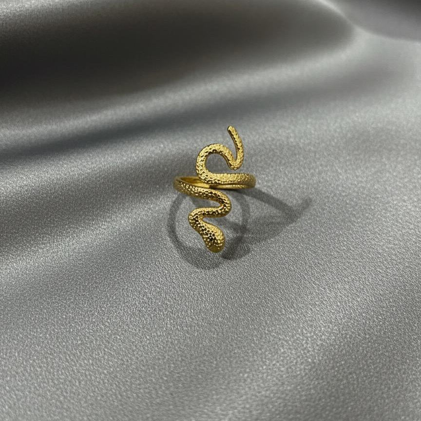 Gold snake-shaped ring on a gray satin surface