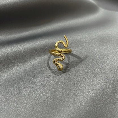 Gold snake-shaped ring on a gray satin surface