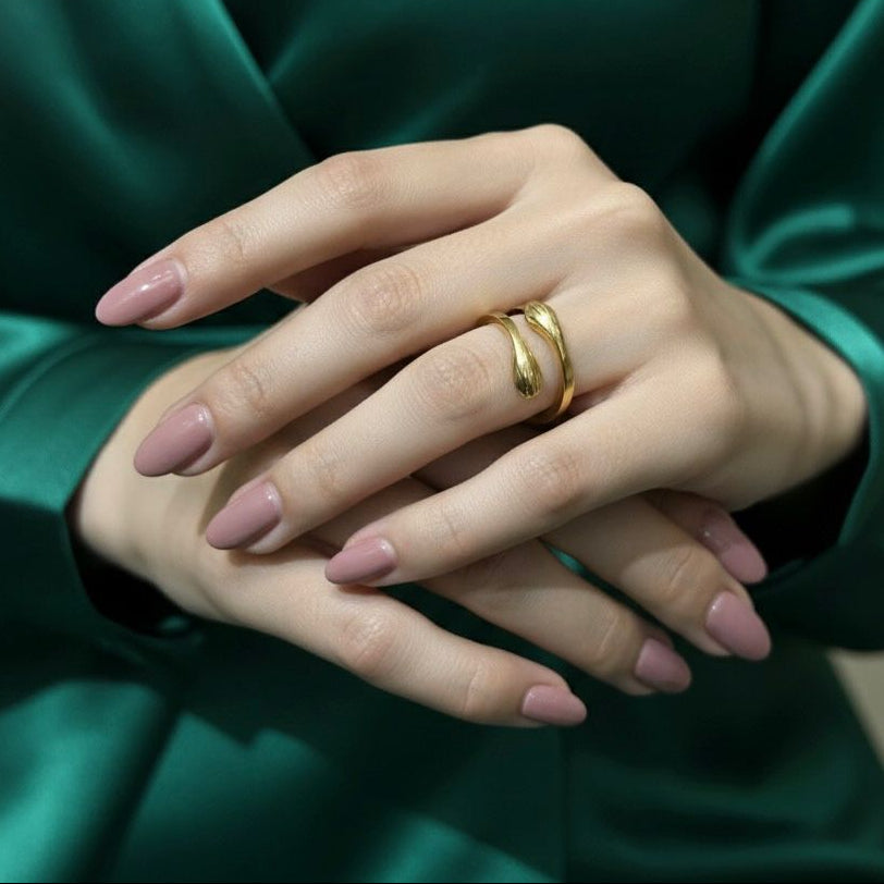 Close-up of a hand wearing a gold ring with a green satin garment in the background
