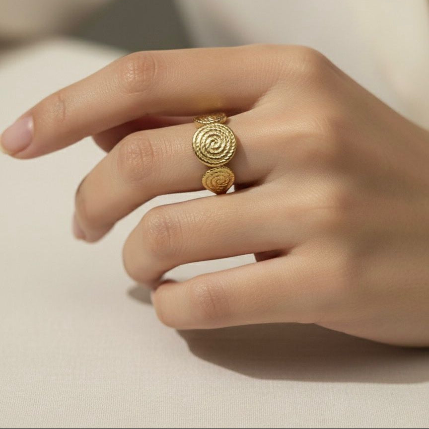 Gold ring with intricate design on a person's finger against a neutral background