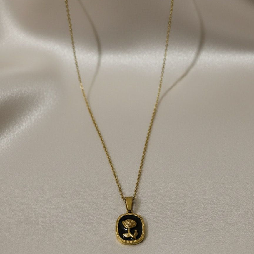 Gold necklace with a black pendant on a light gray background