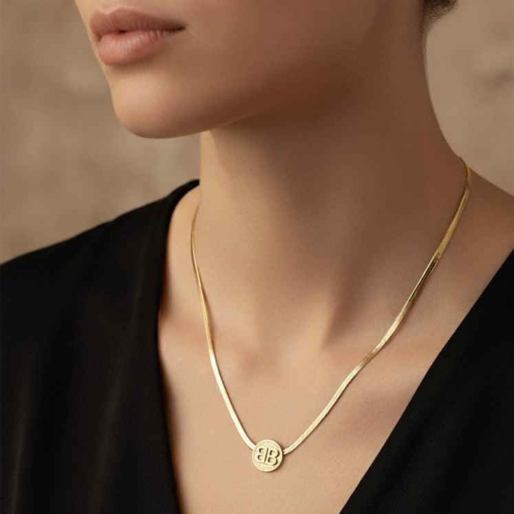 Gold necklace with a round pendant worn by a person against a neutral background