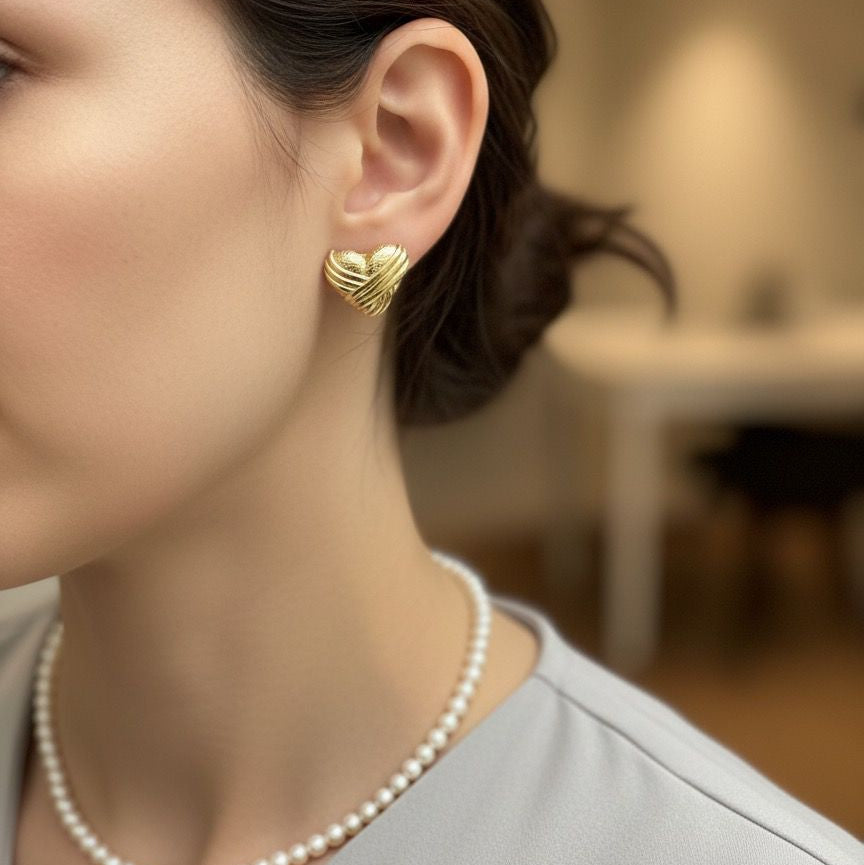 Woman wearing gold heart-shaped earrings with a blurred indoor background